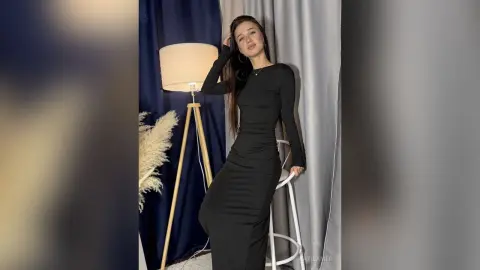 Elegant woman in a sleek black long-sleeve maxi dress posing in a moody studio setting with soft lighting.