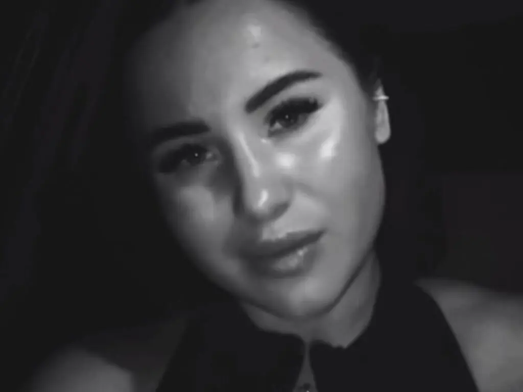 Close-up portrait of a woman in a black outfit with a moody, cinematic black and white aesthetic.