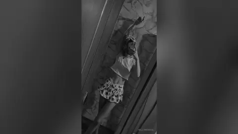 Stylish woman in a white crop top and floral shorts posing against a marble wall in a moody black and white photo.