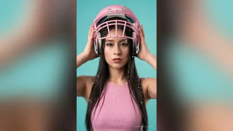 AnnyeWilliams wears a pink football helmet and a pink tank top while posing against a blue background.