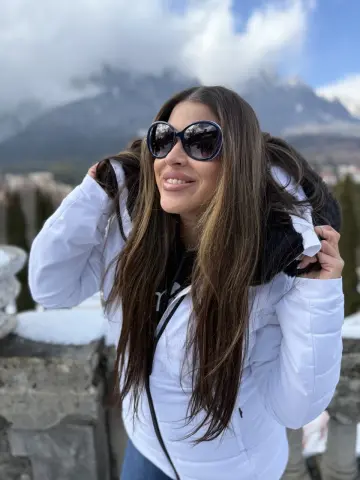 Smiling woman in a white winter jacket and sunglasses enjoying a sunny day in the snowy mountains.