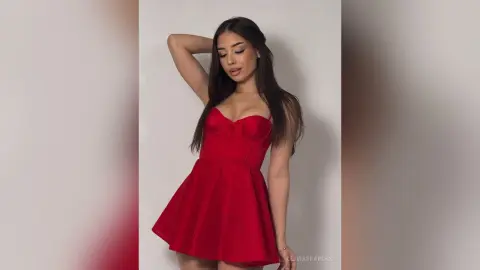Young woman in a chic red mini dress posing against a neutral studio background with a confident mood.