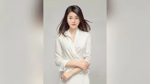 Elegant woman in a white long-sleeve blouse posing against a minimalist grey background with a serene mood.