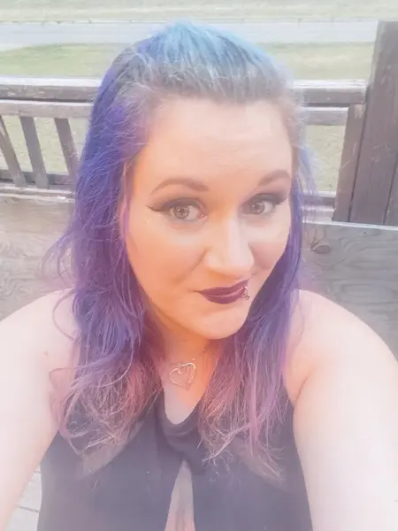 LuxieLuna — LuxieLuna poses with purple hair and dark lipstick, wearing a black halter-style top while looking directly at the camera.