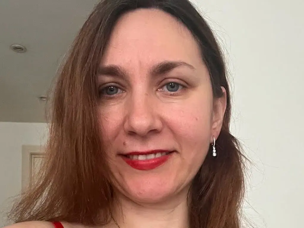 Smiling woman with long brown hair wearing red lipstick in a bright indoor setting.