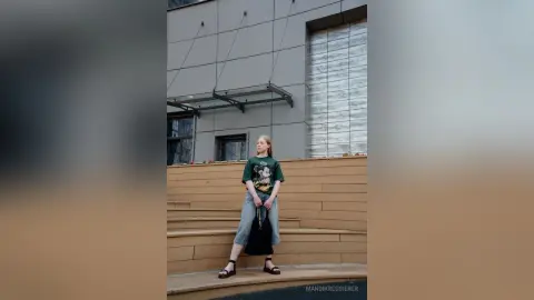 Young woman in a Mickey Mouse graphic tee and denim jeans standing on a wooden terrace by a modern building.