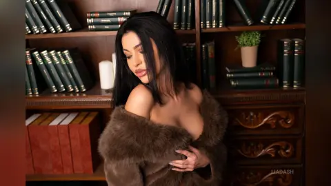 Glamorous woman in a brown faux fur coat posing in a cozy library filled with vintage books.