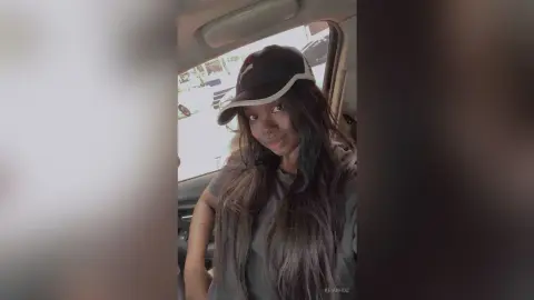 KeianHoz wears a black baseball cap and a dark t-shirt while sitting in a car.