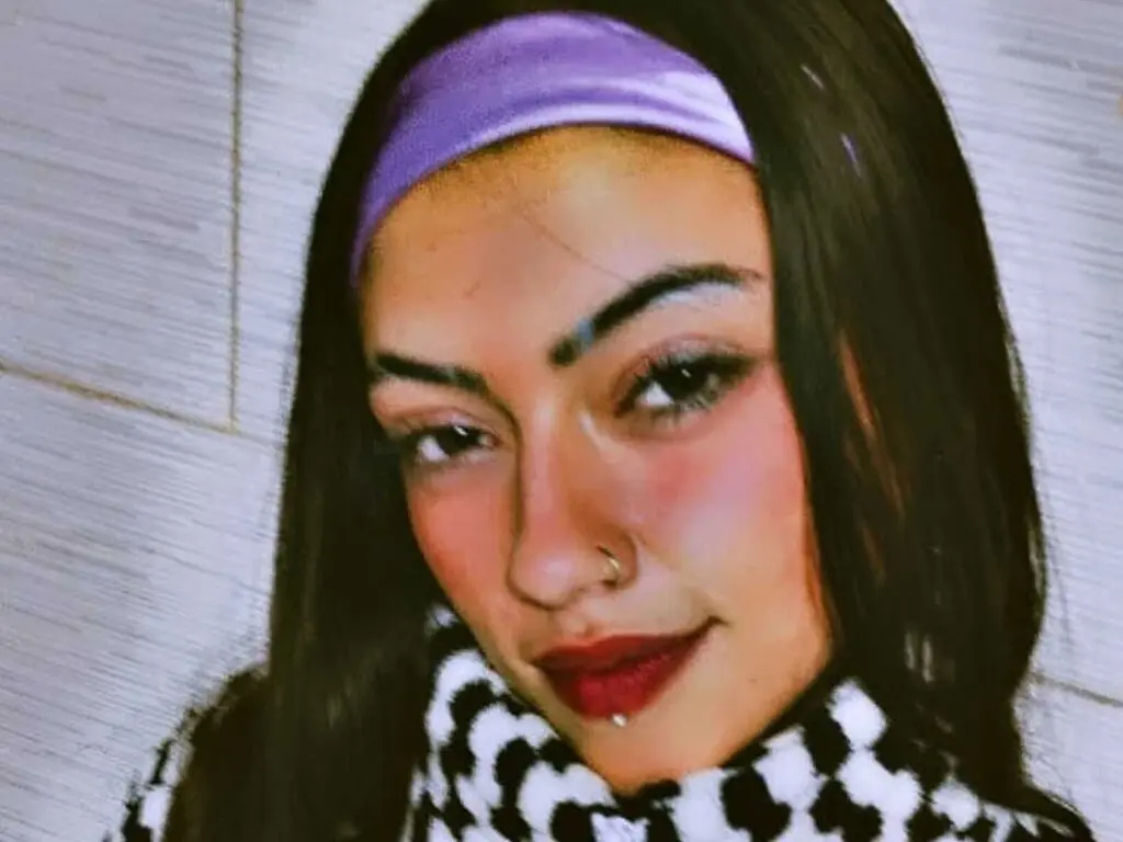 JeanneGerard looks at the camera with long dark hair, a purple headband, and red lipstick, wearing a black and white patterned top.
