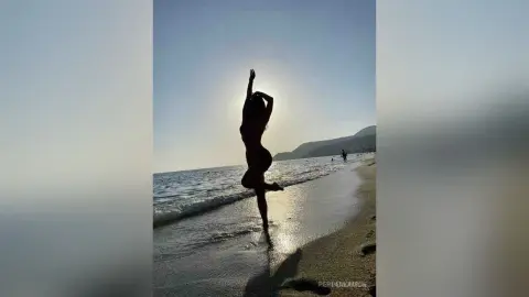 Silhouette of a fit woman in swimwear dancing on a sunny beach at sunset with ocean waves.