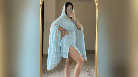 Woman in elegant light blue traditional Indian salwar kameez outfit posing in a mirror for a selfie.