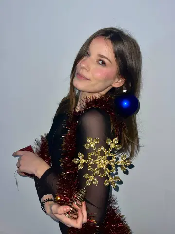 Young woman in a black sheer top draped in red tinsel and gold snowflake ornaments for a festive holiday mood.