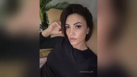Young woman in a black long-sleeve shirt relaxing on a beige sofa in a cozy indoor setting.