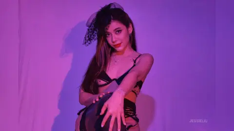 JessieLiu poses in black lace lingerie against a purple background, looking at the camera while holding her thighs.