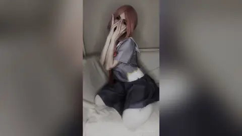 Shy girl in school uniform sitting on a white sofa with pink hair in a soft, moody indoor setting.