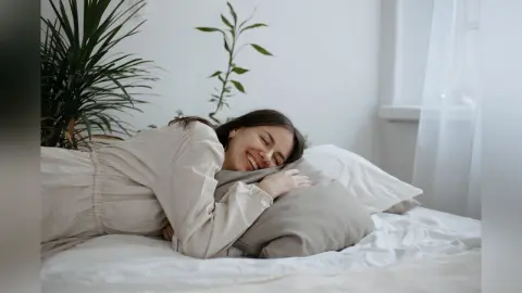 Happy woman in white loungewear relaxing on a bed in a bright, minimalist bedroom.
