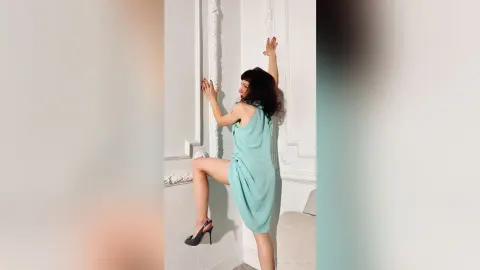 SabrinaBauer — SabrinaBauer poses in a light blue dress and black high heels against a white wall.