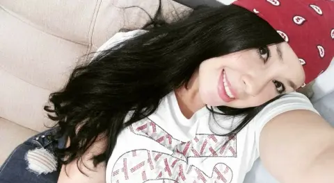 Smiling young woman with long dark hair wearing a white graphic t-shirt and red beanie relaxing on a couch.