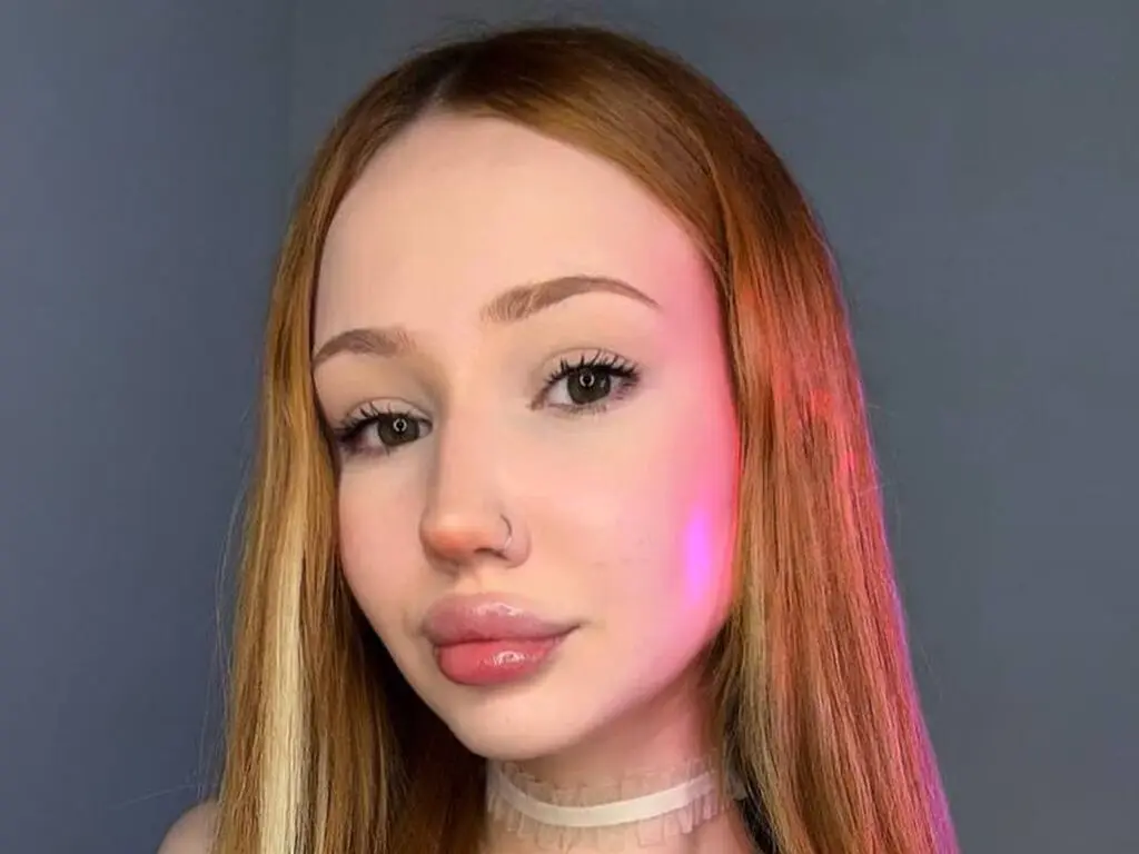 Redheaded woman with natural makeup wearing a white lace choker in soft studio lighting.