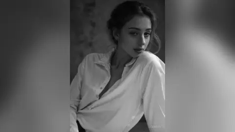Moody black and white portrait of a young woman in a white button-down shirt looking into the camera.