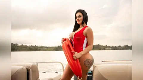 ErikaHoffman stands on a boat wearing a red one-piece swimsuit, holding a red life ring against her body with a lake in the background.