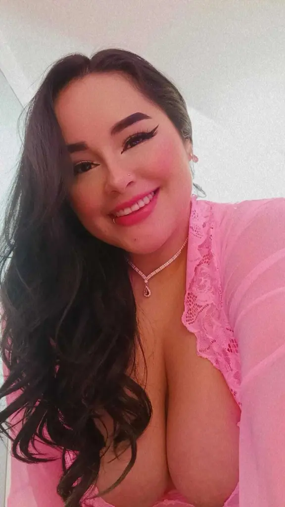 Celesttebeautiful smiles at the camera with long dark hair and a tattoo on her chest while wearing a red top.
