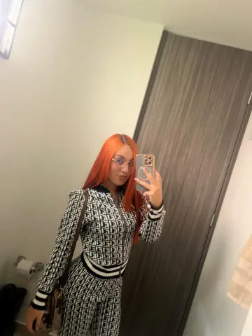 Young woman with bright orange hair wearing a black and white patterned tracksuit in a modern room.