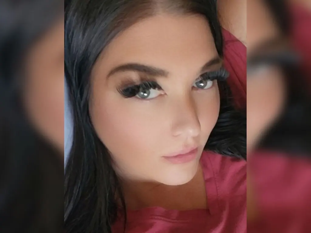 HollyComming looks directly at the camera with long eyelashes and dark hair, wearing a red shirt.
