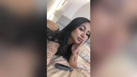 Young woman with long dark hair relaxing on a bed in a cozy, intimate indoor setting.