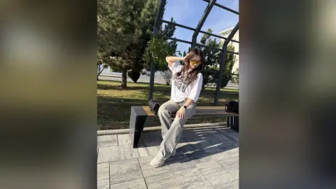 Stylish woman in white t-shirt and grey jeans sitting on a park bench on a sunny day.