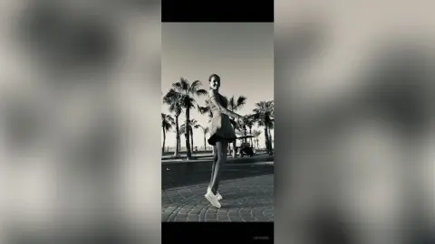 Smiling woman in a summer dress walking through a tropical palm tree resort in a nostalgic black and white style.