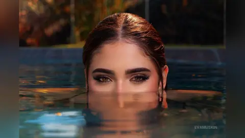 EvaMuskin peeks out from a dark swimming pool with her eyes and forehead visible above the water's surface.