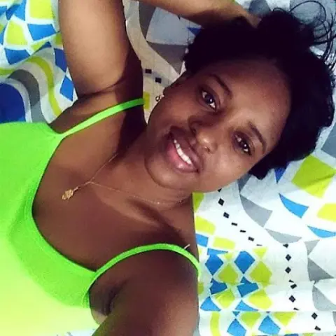 HellenJohansson — Smiling young woman in a bright lime green tank top relaxing on a patterned blue and white bedspread.