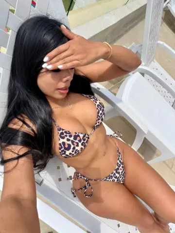Woman in leopard print bikini relaxing on a white lounge chair under bright sunlight.