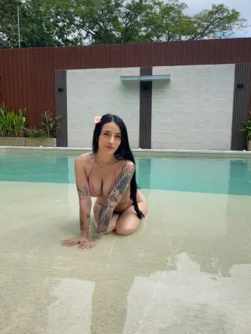 Tattooed woman in a pink bikini relaxing in a luxury swimming pool on a sunny day.