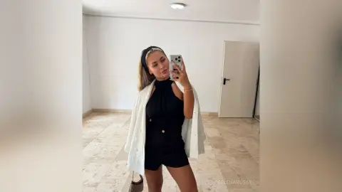 SelenaRusse takes a mirror selfie wearing a black halter romper and a white open shirt.