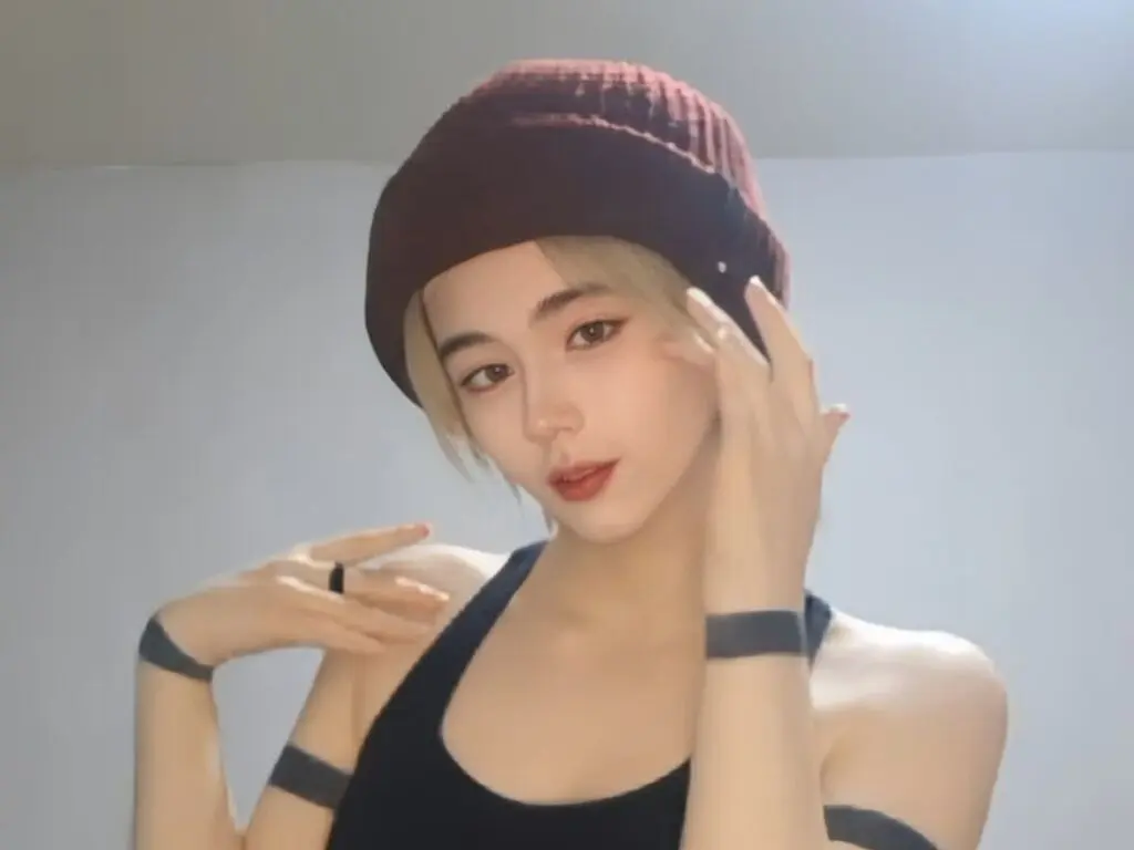 Young woman in a black tank top and burgundy beanie posing with a relaxed mood in a minimalist indoor setting.