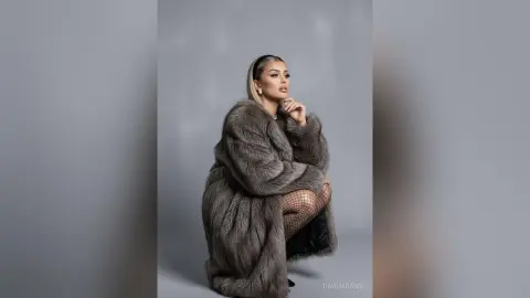 Elegant woman in a luxurious grey faux fur coat posing against a grey studio background with a sophisticated mood.