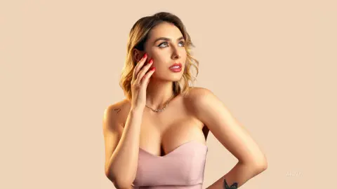 Elegant woman in a pink strapless top posing with a dreamy expression against a neutral beige background.