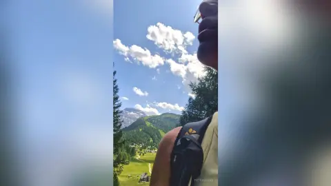 Man with backpack looking at scenic green mountains and blue sky during a summer hiking trip.