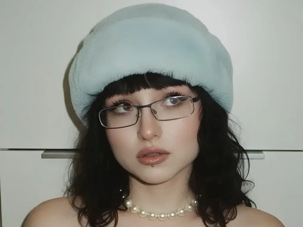 Young woman with dark hair and glasses wearing a light blue beret and pearl necklace in a soft aesthetic mood.
