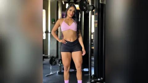 Athletic woman in pink sports bra and black shorts posing confidently in a modern gym setting.