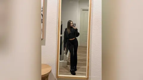 EvelynMills poses for a mirror selfie wearing a black long-sleeve crop top and black leggings.