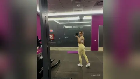 Fit woman in yellow gym set taking a mirror selfie in a modern purple fitness studio.