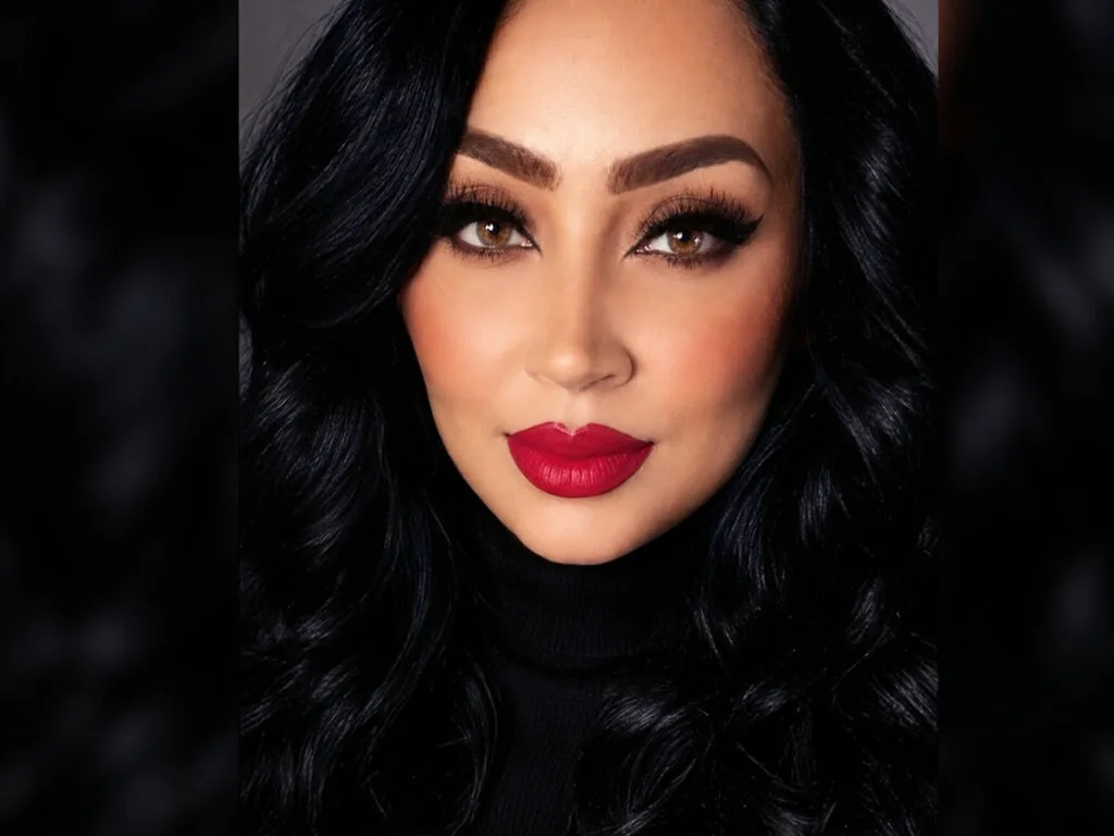SharlinMoreva poses with long wavy black hair and bold red lipstick.