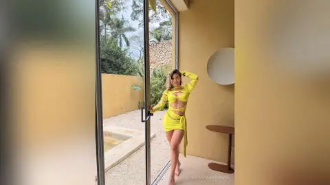Stylish woman in a bright yellow cutout maxi dress standing in a modern sunlit patio setting.