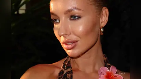 Glamorous woman with glowing makeup and gold hoop earrings wearing a leopard print top in a tropical night setting.