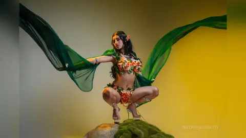 Ethereal elf woman in a floral fantasy outfit posing with flowing green fabric in a magical studio setting.