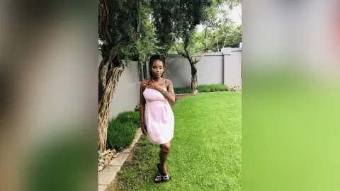 Young woman in a pink summer dress standing on a green lawn in a sunny garden setting.