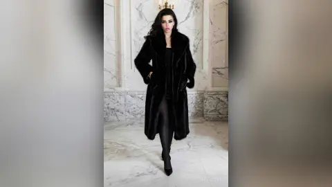 Elegant woman in a luxurious black faux fur coat standing in a sophisticated marble interior.